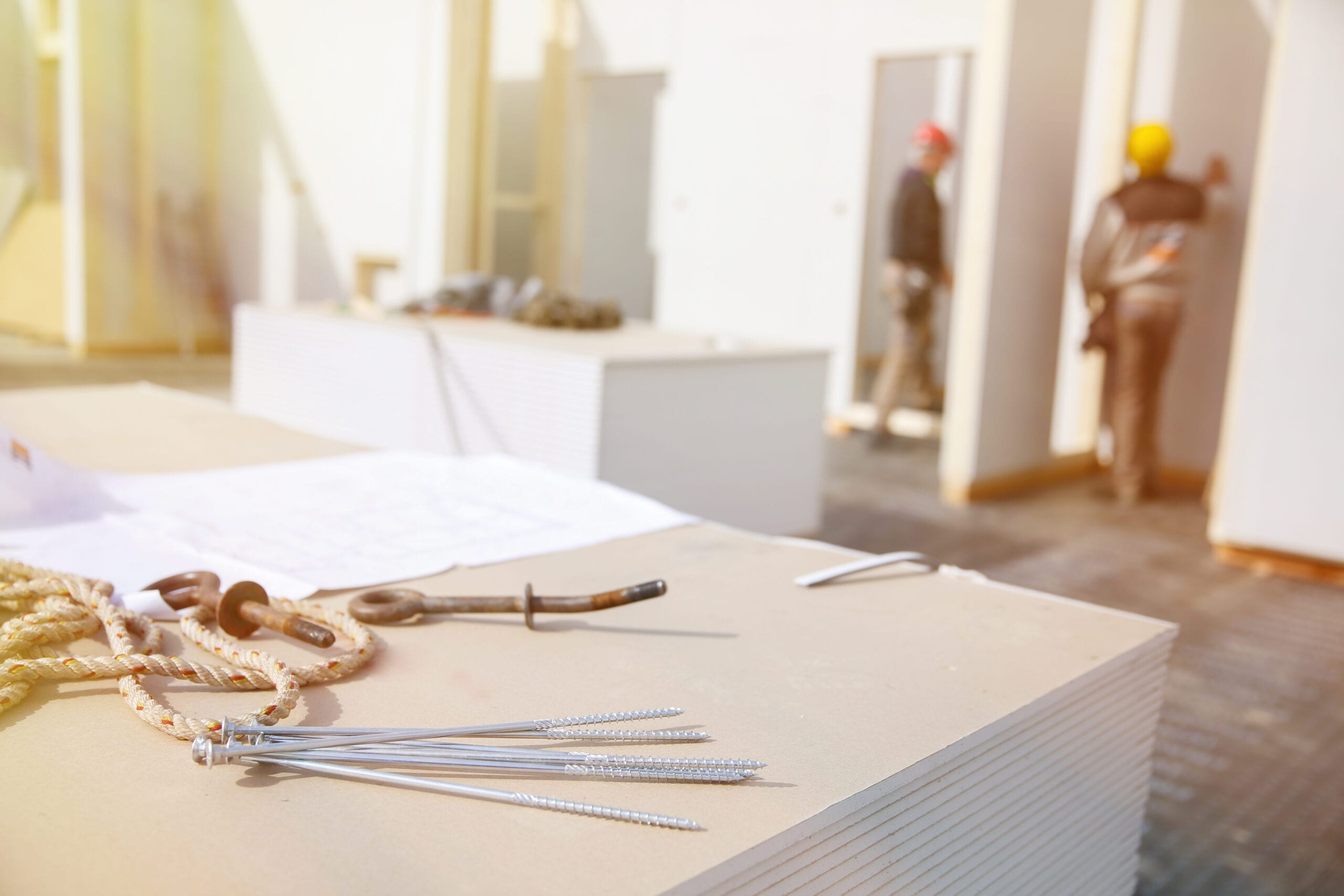 Building plan, eye bolt and screws on plasterboard panels with workers in background